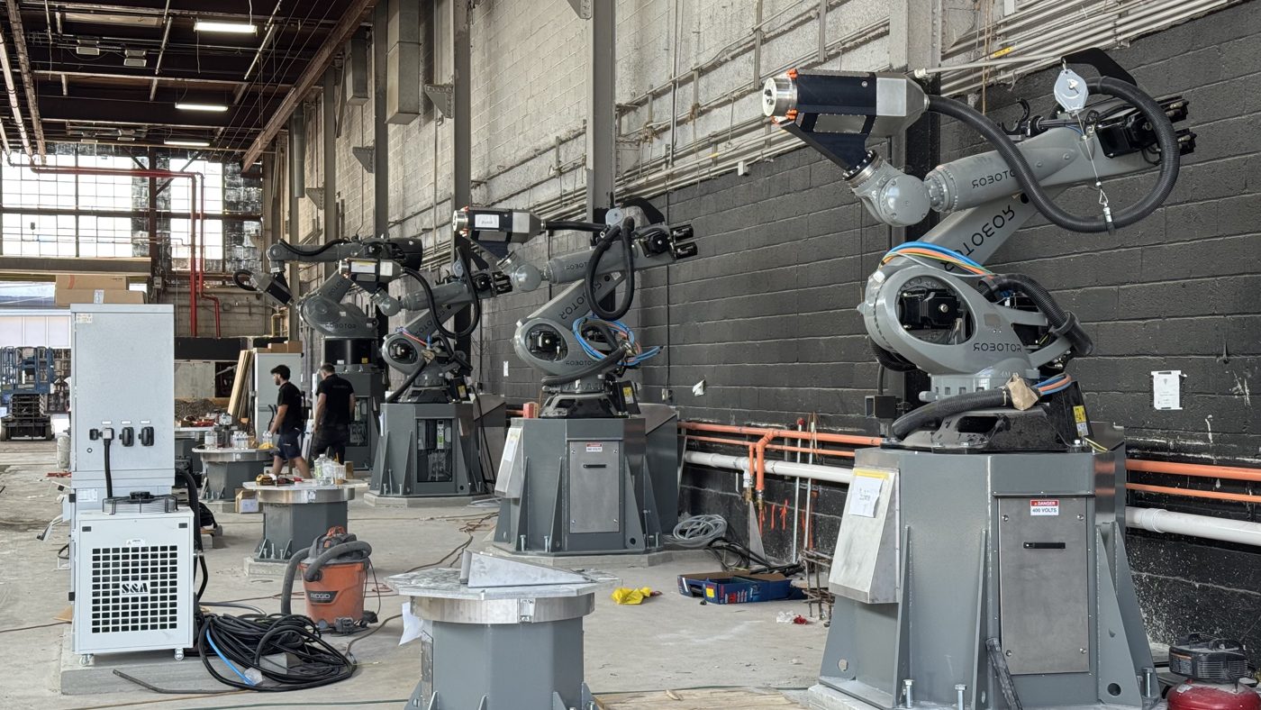 Industrial robot arms on pedestals in a large warehouse workshop.
